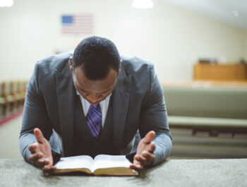 An African-American male praying with his head down looking at the Bible at the church